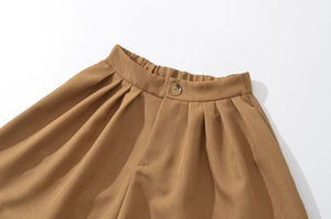 Detail of tan casual shorts featuring elastic waist, pleated front, and amber-toned button
