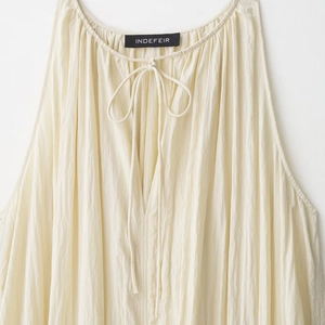 Beige halter neck top with pleated texture and thin neck ties on white background