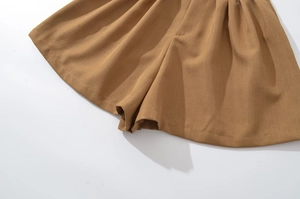 Detailed close-up of brown pleated cotton twill shorts with a high-waisted A-line cut