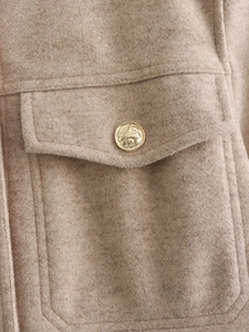 Macro shot of oatmeal tweed jacket texture showing chest pocket and gold embossed button
