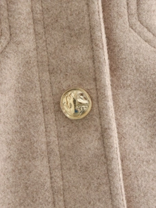 Macro shot of gold vintage button and fine stitching on camel wool blend jacket