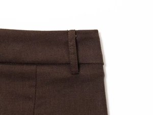 Detailed macro view of dark brown woven trousers showing belt loops and precise stitching