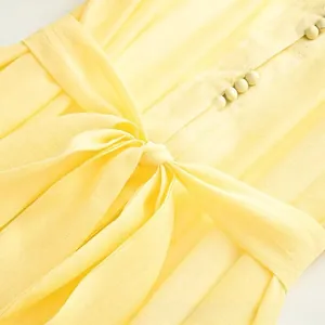 Détail de robe jaune avec un nœud à la taille et des boutons recouverts assortis
