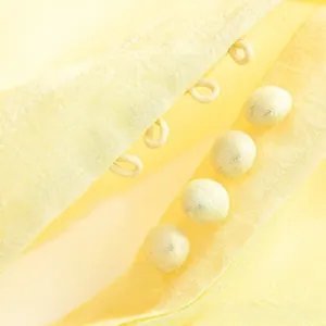 Détail du tissu d'une robe jaune avec quatre boutons recouverts et une texture tissée