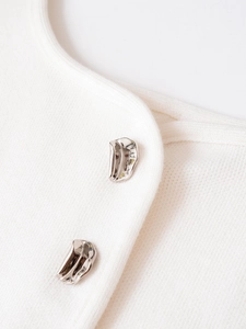 Detail of white knit sweater featuring irregular silver mirror metal buttons and texture