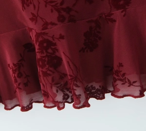 Detail of burgundy floral flocked mesh fabric with ruffled lettuce edge design