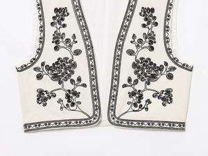 Détail du gilet crème avec broderie florale noire complexe et tissu tissé texturé