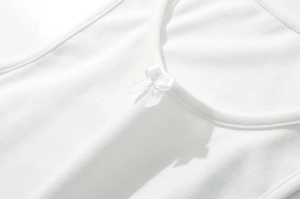 Dettaglio dello scollo di un gilet in maglia bianca con un piccolo fiocco di seta
