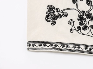 Vue macro des broderies noires et de la texture du tissu crème sur le gilet