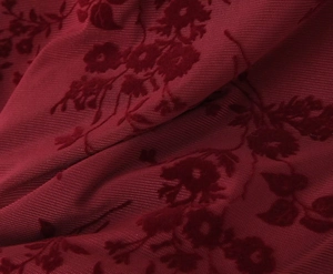 Detailed close-up of dark red floral flocked tulle fabric with soft velvet rose patterns