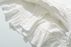 Dettaglio dell'abito in maglia a costine bianche con balze sovrapposte e pantaloncini interni