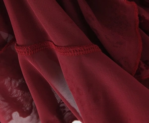 Detailed close-up of burgundy mesh fabric with floral flocking and overlock stitching