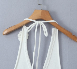Detail of white knit halter top featuring irregular texture and 3D floral accent