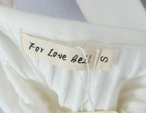 Macro shot of white ribbed knit fabric texture with stitched brand neck label and size S