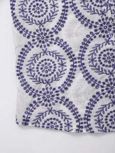 Detail of white shirt featuring purple floral embroidery and matching round buttons