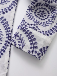 Close-up of intricate blue floral embroidery and eyelet details on white cotton shirt sleeve