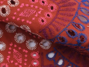 Dettaglio del ricamo inglese rosso mattone con motivi floreali multicolori vivaci