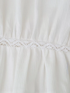 Dettaglio del tessuto plissettato bianco con elegante ricamo geometrico in pizzo