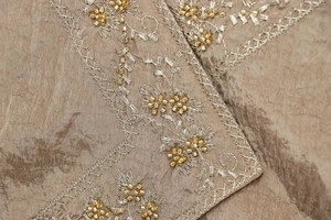 Macro shot of gold floral embroidery and hand-sewn beads on the silk tank top