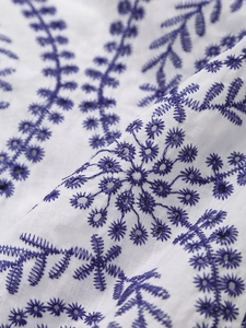 Detail of white cotton fabric with blue floral embroidery and intricate needlework