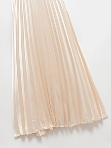 Close-up of champagne gold pleated skirt with silky satin texture and vertical pleats