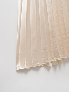 Close-up of champagne pleated satin skirt showing elegant fabric texture and drape