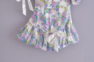 Detail of floral dress showing white lace bow, blue flower print and ruffled hem texture