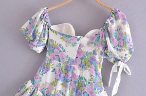 Detail of floral print dress featuring puff sleeves and bow tie cuffs on white fabric