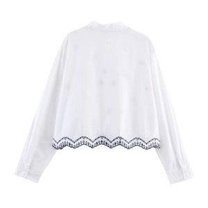 Détail de la broderie ajourée bleu marine et de l'ourlet festonné sur la chemise blanche