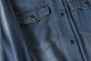 Detailed view of blue denim shirt fabric texture with flap pocket and black snap button