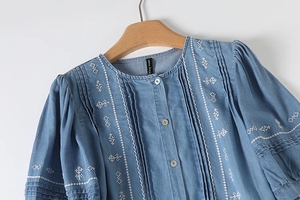 Detailed view of white geometric embroidery and pleats on a blue denim dress