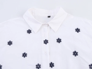 Détail du col d'une chemise en popeline blanche avec broderies florales bleues et boutons