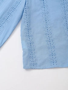 Detail of light blue shirt featuring vertical eyelet embroidery and floral lace patterns