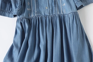 Close-up of white geometric embroidery and pleated waist detail on light blue denim dress