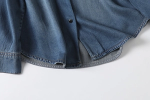 Close-up of curved hem and stitching detail on a washed blue denim shirt for women