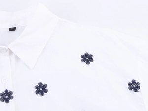 Vue détaillée de la broderie marguerite bleu foncé et de l'étiquette sur la chemise blanche