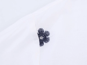 Gros plan détaillé sur la broderie florale bleue et l'œillets sur la chemise en popeline