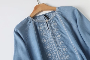 Detail of white ethnic embroidery and wooden button on light blue cotton blouse