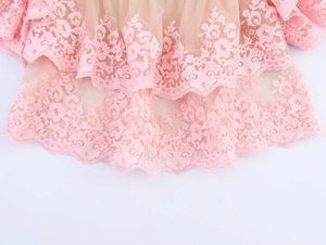 Close-up of pink floral embroidery lace and tiered mesh ruffles on a summer top