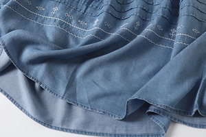 Detail of light blue denim hem featuring white embroidery and pleated design