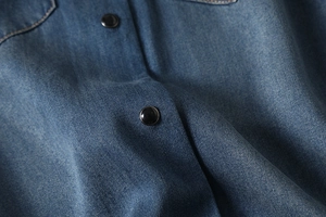 Detailed close-up of blue denim fabric texture and black button on a long-sleeve shirt