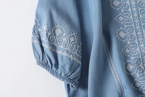 Detailed view of white geometric embroidery on light blue cotton shirt sleeve