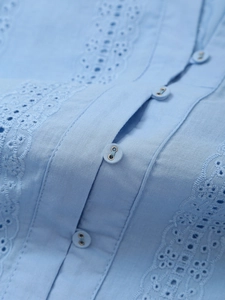Macro detail of light blue shirt featuring hollow lace embroidery and matching small buttons