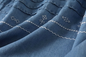 Detailed close-up of blue denim fabric with intricate white floral embroidery patterns