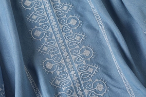 Detail of white ethnic embroidery on a blue cotton shirt with a loose fit texture