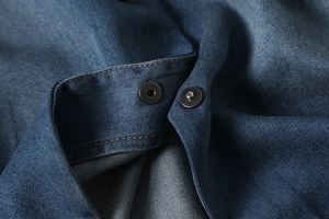 Detail of dark blue denim fabric texture and black metal magnetic snap button closure