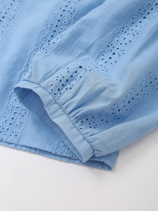 Macro detail of light blue sleeve with geometric eyelet embroidery and pleated cuff