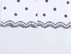 Détail de chemisier blanc en coton avec broderie florale bleue et bord festonné