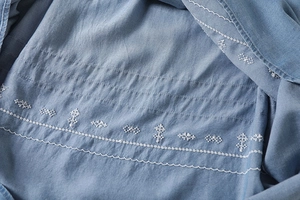 Macro shot of light blue denim fabric with white embroidery and fine pintuck detailing