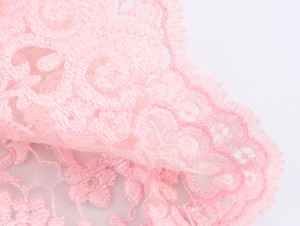 Macro shot of light pink lace top showing detailed floral embroidery and ruffled mesh layers